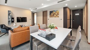 A modern hotel room with a dining area, a sofa, a TV, and a painting on the wall. - Regal Residences Tay ho (Hanoi)