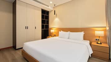 A hotel room with a large bed, two bedside tables with lamps, a wardrobe, and a built-in shelf unit.