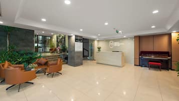 A hotel lobby with a reception desk, seating area, piano, and a staircase leading to an upper floor.