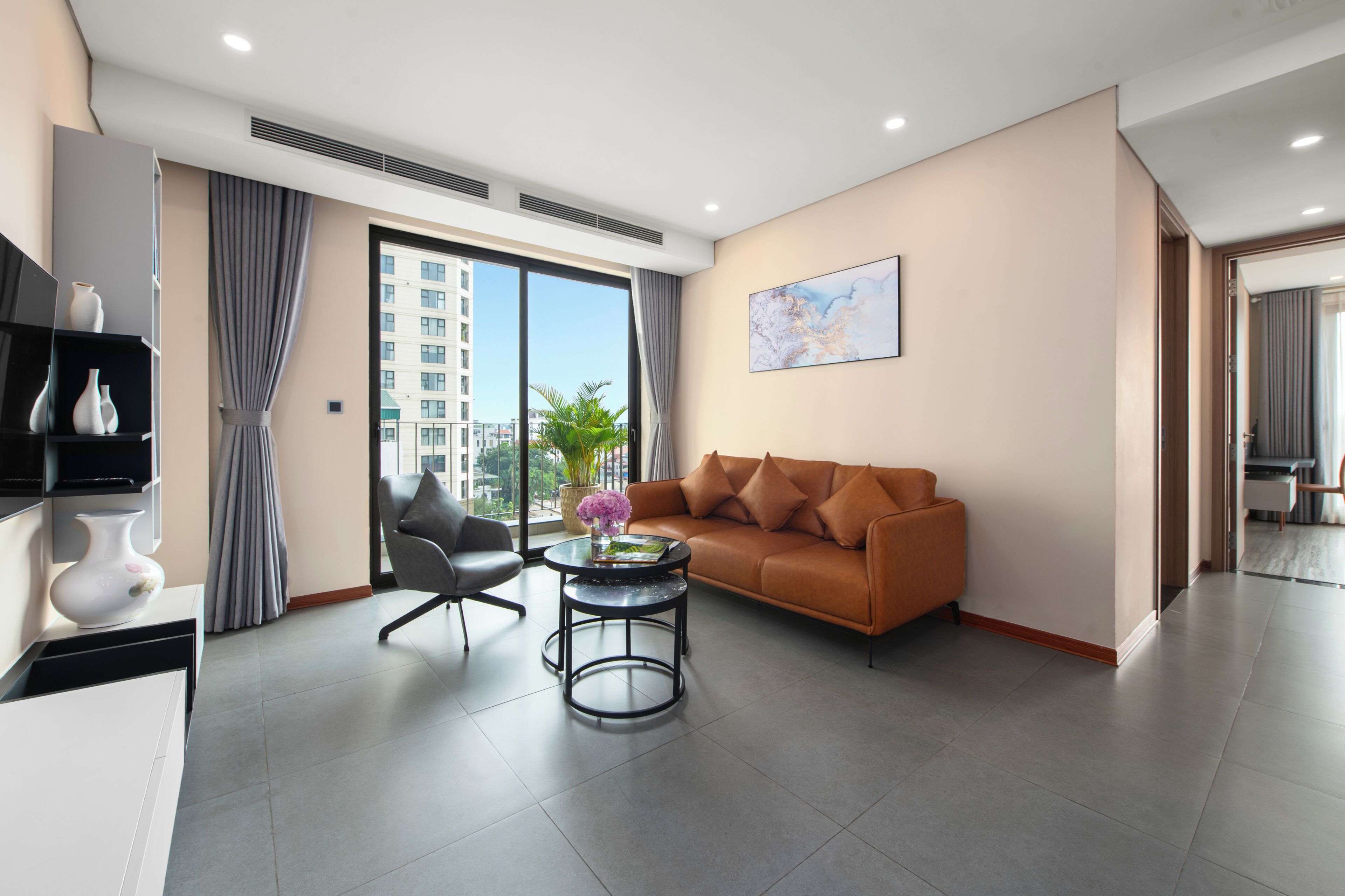 A modern living room with a sofa, armchair, and coffee table. There is a large window with a view of buildings outside.