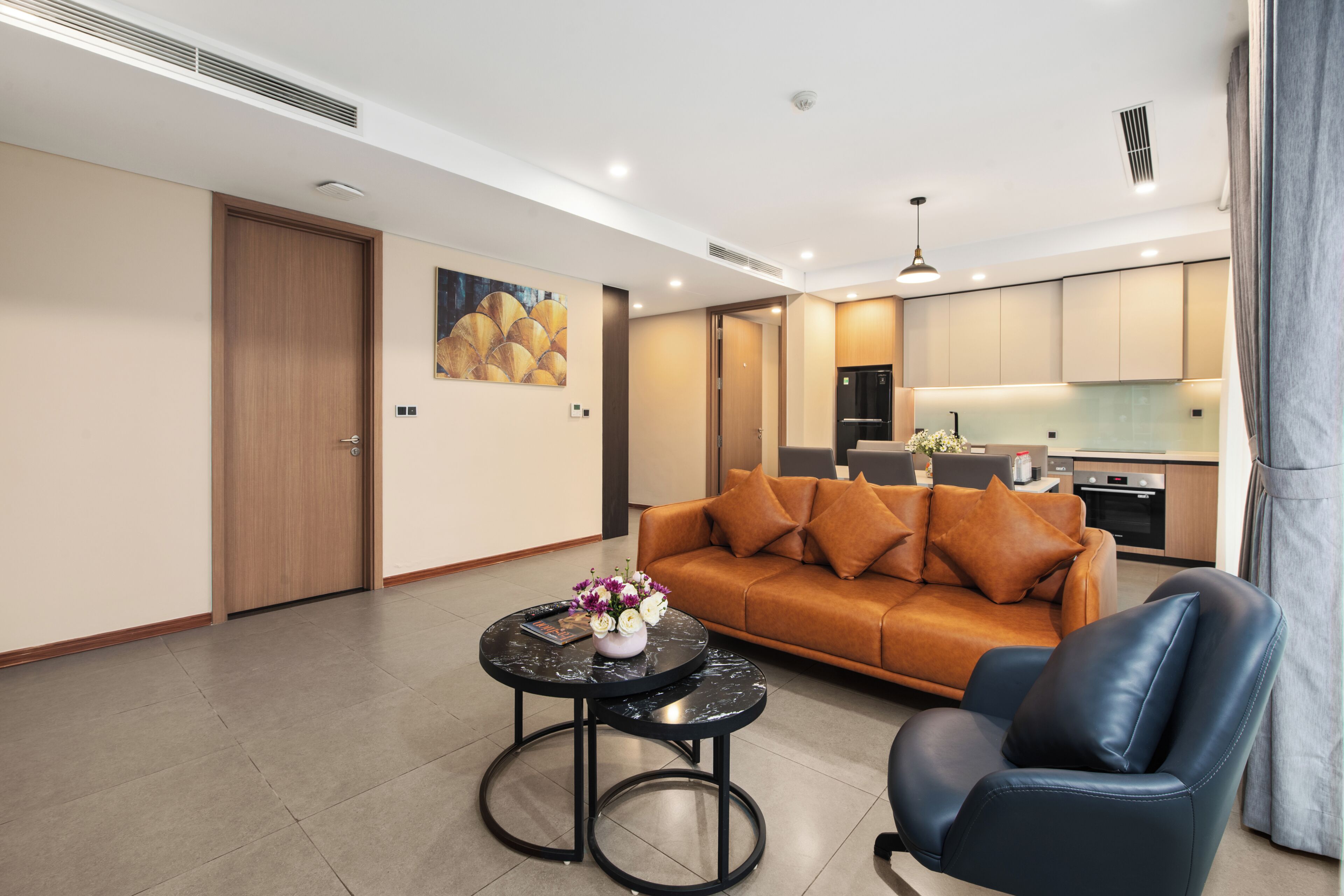 A modern living room with a sofa, a coffee table, and a chair. There is a kitchen area in the background.