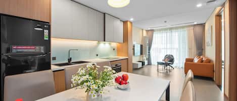 A modern kitchen with a built-in LG refrigerator, a dining area with a white table, and a living room with a sofa and a TV.