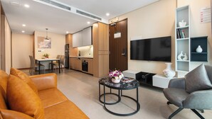 A modern living room with a sofa, a coffee table with a vase, a grey armchair, a flat-screen TV, and a bookshelf. - Regal Residences Tay ho (Hanoi)