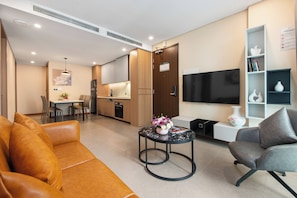 A modern living room with a sofa, a coffee table with a vase, a grey armchair, a flat-screen TV, and a bookshelf. - Regal Residences Tay ho (Hanoi)