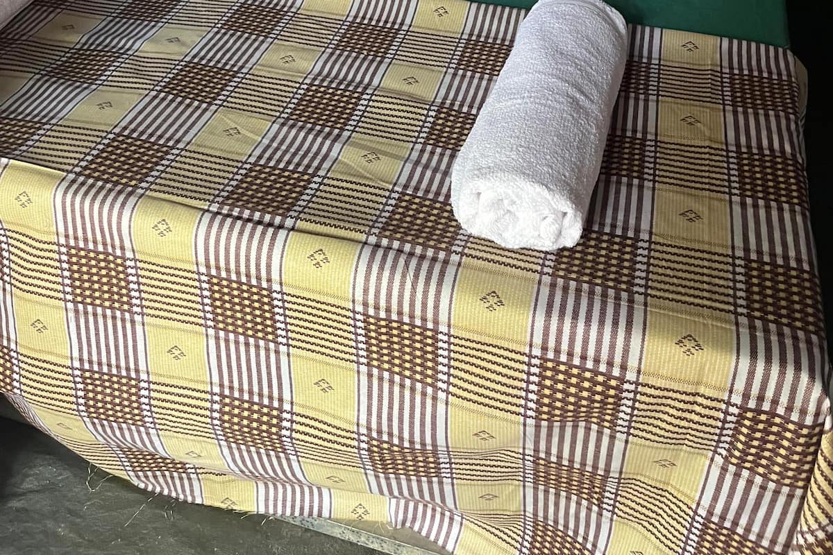 Una carpa con dos camas, cada una con sábanas verdes y almohadas rojas. Una toalla enrollada está en la cama inferior.