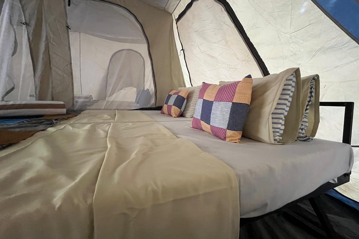Una tienda de campaña con una cama en su interior, que incluye un colchón color arena, un edredón y varias almohadas.