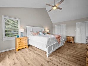 A bedroom with a bed, wooden nightstands, a ceiling fan, a window with blinds, and a closet.