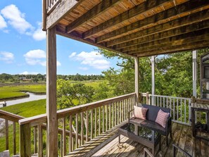 A wooden deck with a bench and railing, overlooking a green landscape with a river.