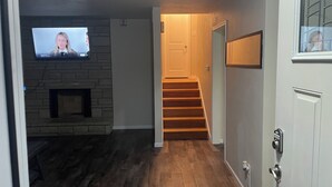 A living room with a stone fireplace, a TV mounted on the wall, and a staircase leading to another room. - Charming 2-bedroom house in Jefferson City with AC (Jefferson City)