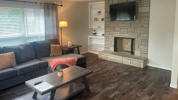 A living room with a sofa, a coffee table, a fireplace, a TV, and a lamp. - Charming 2-bedroom house in Jefferson City with AC (Jefferson City)