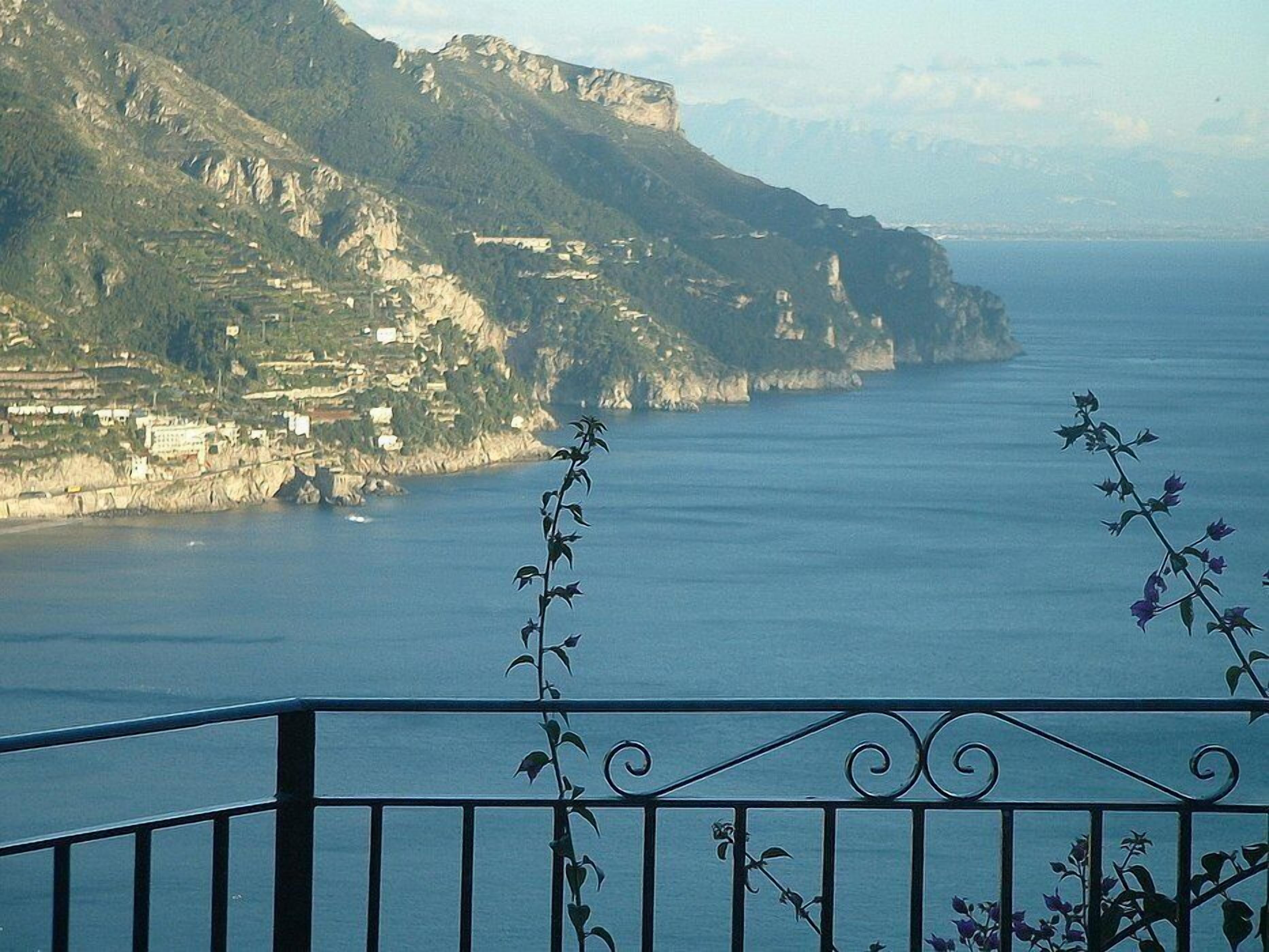A coastal view with a balcony railing and a mountainous backdrop.