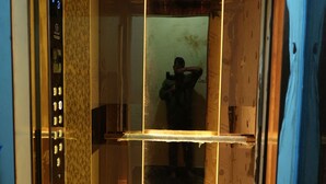 An elevator interior with a patterned wall, a control panel, and a person standing in the center. - Serene Legacy Park View (Mysore)