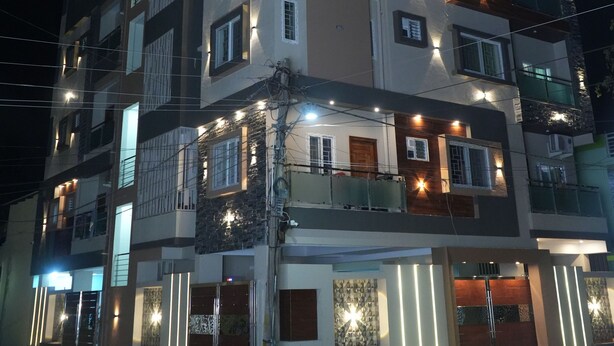 A multi-story building with balconies, a gated entrance, and exterior lighting. - Serene Legacy Park View (Mysore)