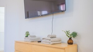 A modern room with a flat-screen TV mounted on the wall, a wooden cabinet with towels, and a small plant.