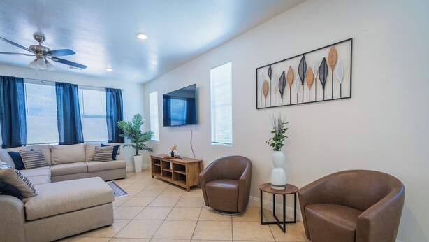 A spacious living room with a beige sofa, two brown leather armchairs, a wooden coffee table, and a ceiling fan.