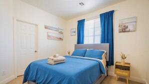 A bedroom with a bed, a nightstand, a window with curtains, and wall art.