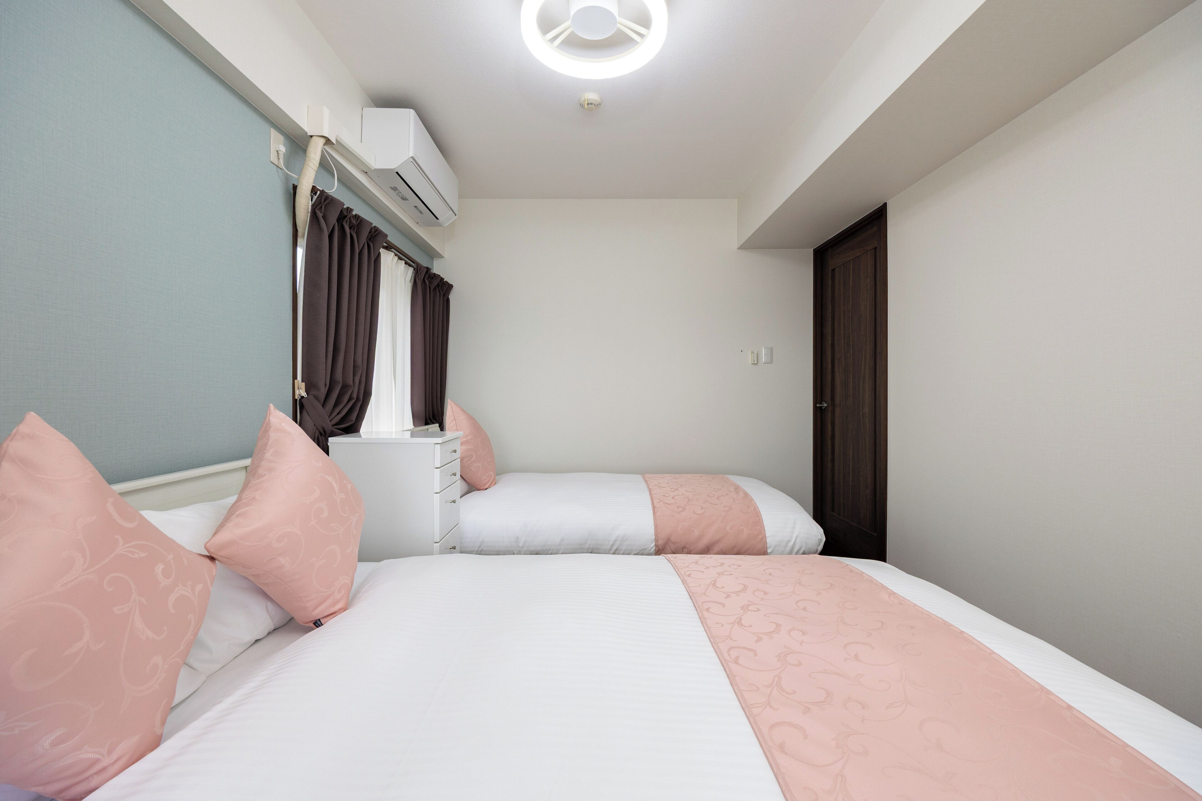 A bedroom with two beds, a nightstand, and a window with curtains.
