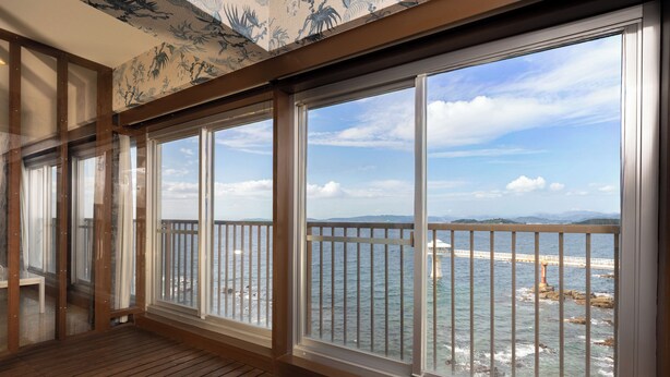 Una stanza con ampie finestre che si affacciano sulla costa, completa di un pontile in legno e vista sul mare e su un ponte.