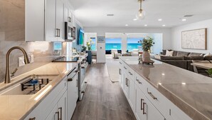 A modern kitchen with a large island, white cabinetry, and a view of the ocean.