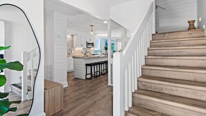 A modern kitchen with white cabinetry, a wooden staircase, and a view into the living area.