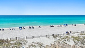 A beach with a wooden fence, beach chairs, umbrellas, and a wooden walkway leading to the beach.