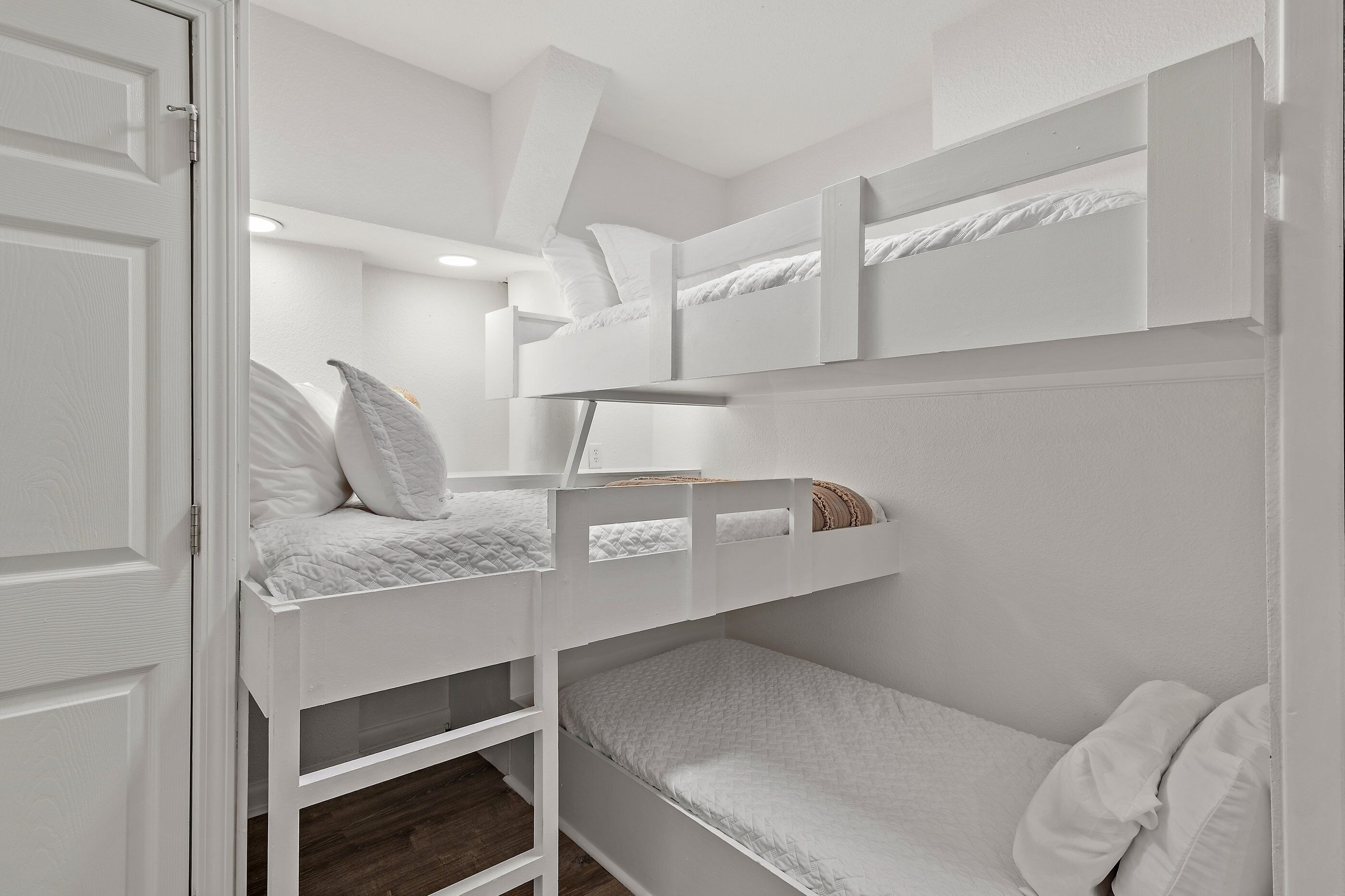A bunk bed room with white bedding and a door.