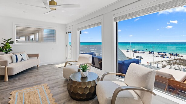 A modern living room with a view of the beach, a ceiling fan, and a large window.