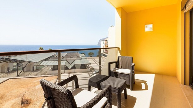 A balcony with wicker furniture, a view of the sea, and a yellow wall. - GuestReady – Madeira escape with ocean view (Funchal)