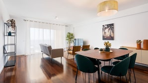 A modern dining area with a wooden table, green chairs, and a hanging light fixture. - GuestReady – Madeira escape with ocean view (Funchal)