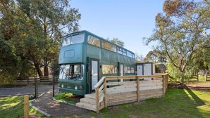 A green double-decker bus parked in a grassy area with a wooden ramp leading up to it.