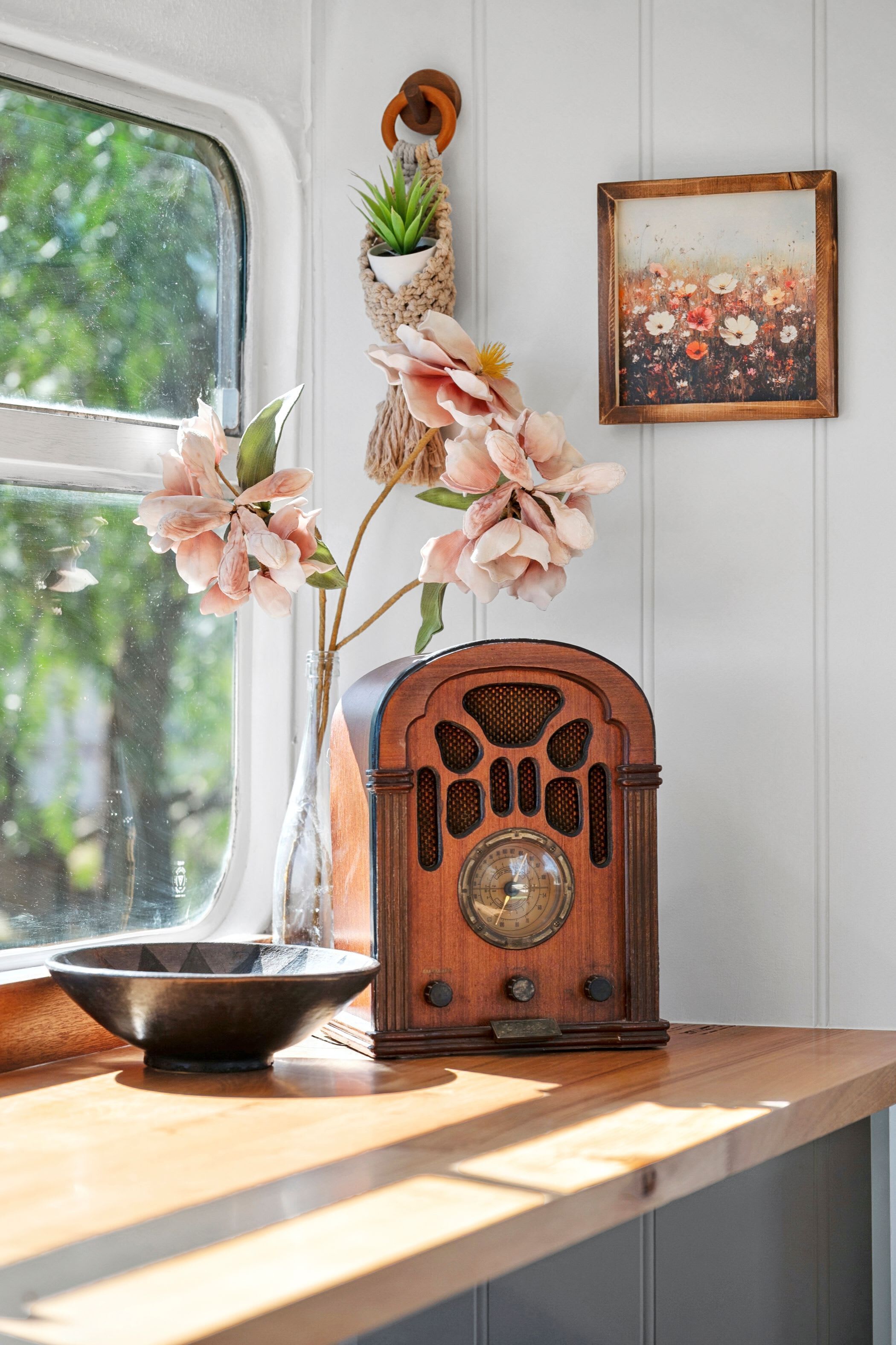 A vintage radio on a wooden countertop, a vase with flowers, and a framed picture on the wall.