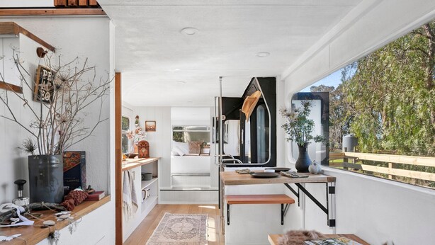 A modern interior with a kitchen, dining area, and a large window offering a view of greenery.