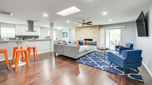 Una sala moderna con un sofá gris, sillones azules y taburetes naranja.