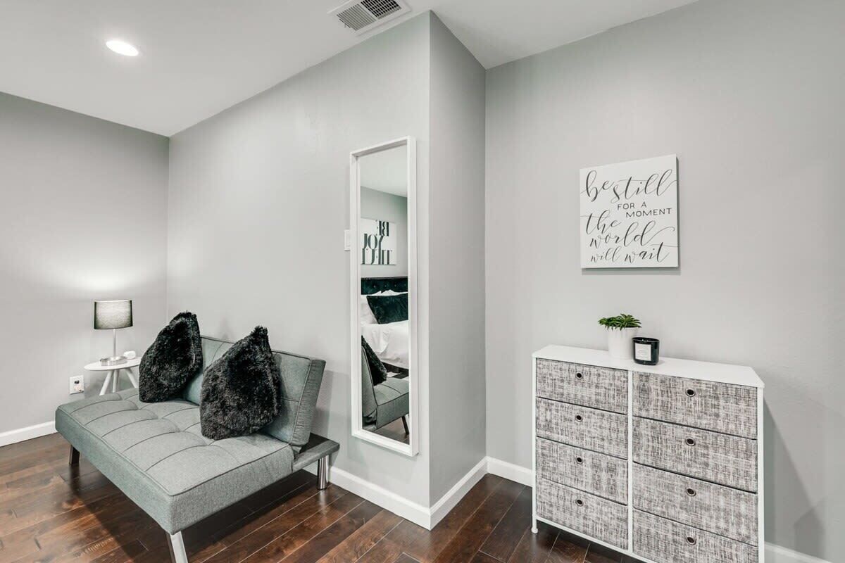 Een moderne woonkamer met een grijze bank, een spiegel, een wit kastje en een motiverende quote op de muur.