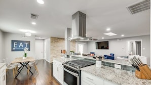 Una cocina moderna con una isla central, electrodomésticos de acero inoxidable y un comedor con mesa y sillas.