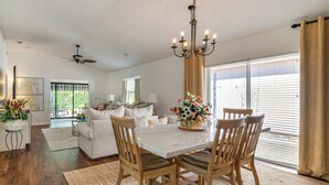 A spacious living room with a dining area, featuring a large window, a chandelier, and a ceiling fan. - Private Pool & Golf Cart! Villa By Spanish Springs (The Villages)