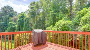 Um deck de madeira com mesa coberta, rodeado por um corrimão vermelho, com vista para uma floresta densa.