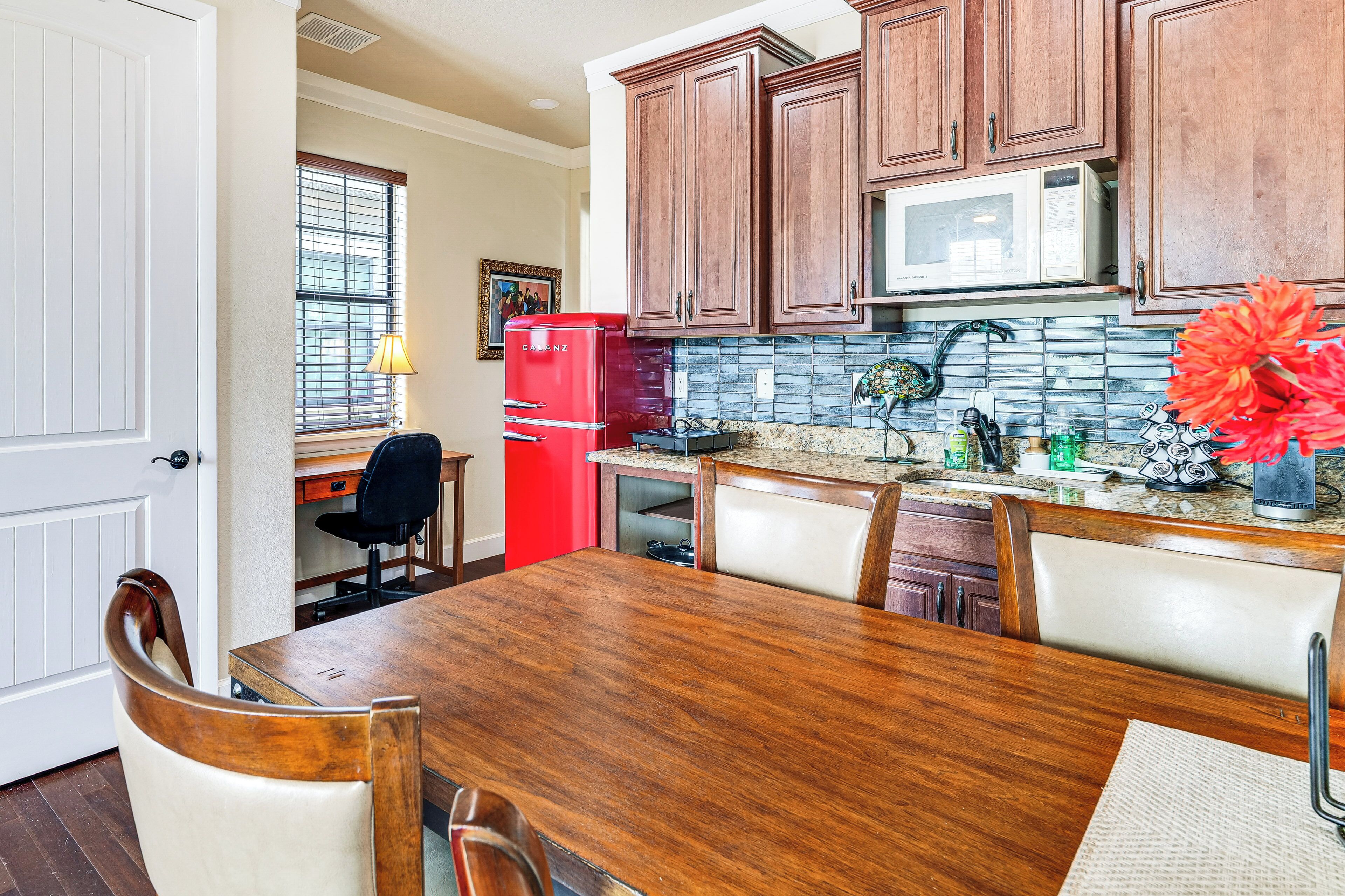 A kitchen with wooden cabinets, a red refrigerator, a dining table with chairs, and a backsplash.