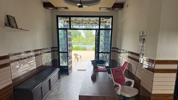 Une pièce avec un bureau en bois, une chaise rouge, un banc et, à travers une porte vitrée, une vue sur un espace extérieur comprenant une chaise et un ordinateur portable.