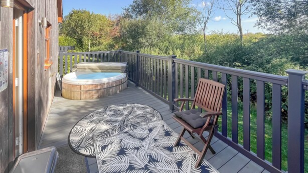 A wooden deck with a hot tub, a patterned rug, and a wooden chair. - You’ll love the spacious layout, perfect for families or groups. (Brigg)