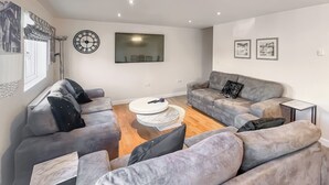 A modern living room with grey sofas, a round coffee table, and a flat-screen TV mounted on the wall. - You’ll love the spacious layout, perfect for families or groups. (Brigg)