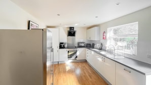 A modern kitchen with white cabinets, a stainless steel refrigerator, a built-in oven, and a window with a view of greenery. - You’ll love the spacious layout, perfect for families or groups. (Brigg)