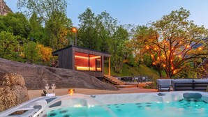 Area idromassaggio con una terrazza in legno e posti a sedere, circondata da alberi e un edificio moderno con ampie finestre.