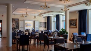 Un'ampia sala da pranzo con numerosi tavoli e sedie, eleganti lampadari e ampie finestre con tende.
