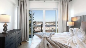 Habitación de hotel con cama, cómoda y vista panorámica de la ciudad a través de amplias ventanas.