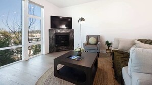 Una sala de estar moderna con chimenea, televisor de pantalla plana y un ventanal con vistas al exterior.