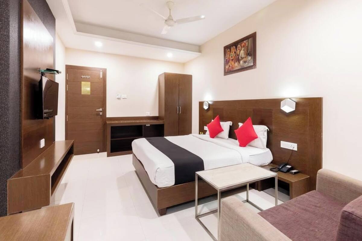 A hotel room with a bed, bedside table, chair, wardrobe, TV, and ceiling fan.