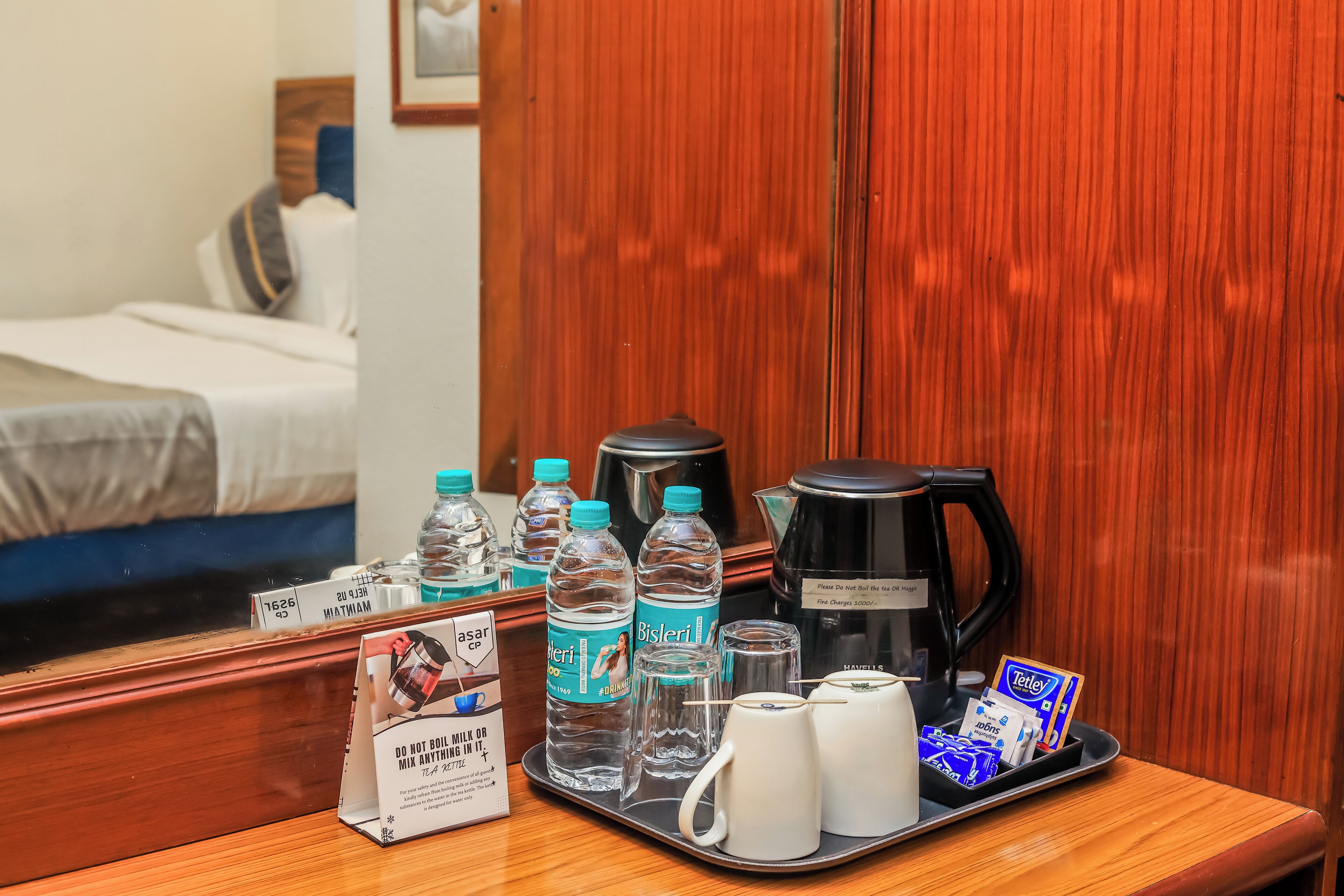 A hotel room with a wooden table set with water bottles, a coffee maker, and a tray with tea bags and glasses.