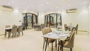 A dining area with multiple tables and chairs, air conditioning units, and a glass partition wall. - asar CP Outer Circle by Orion Hotels (New Delhi)