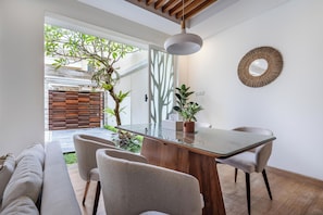 Un espace repas moderne avec une table à plateau en verre, deux chaises, un plafond en bois et une plante en pot.